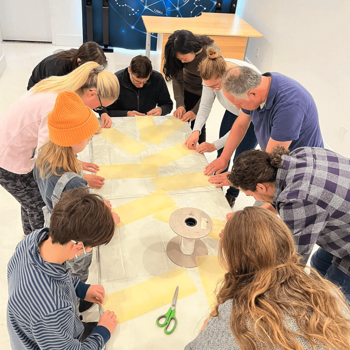 10 people gathered around a table rolling beeswax candles